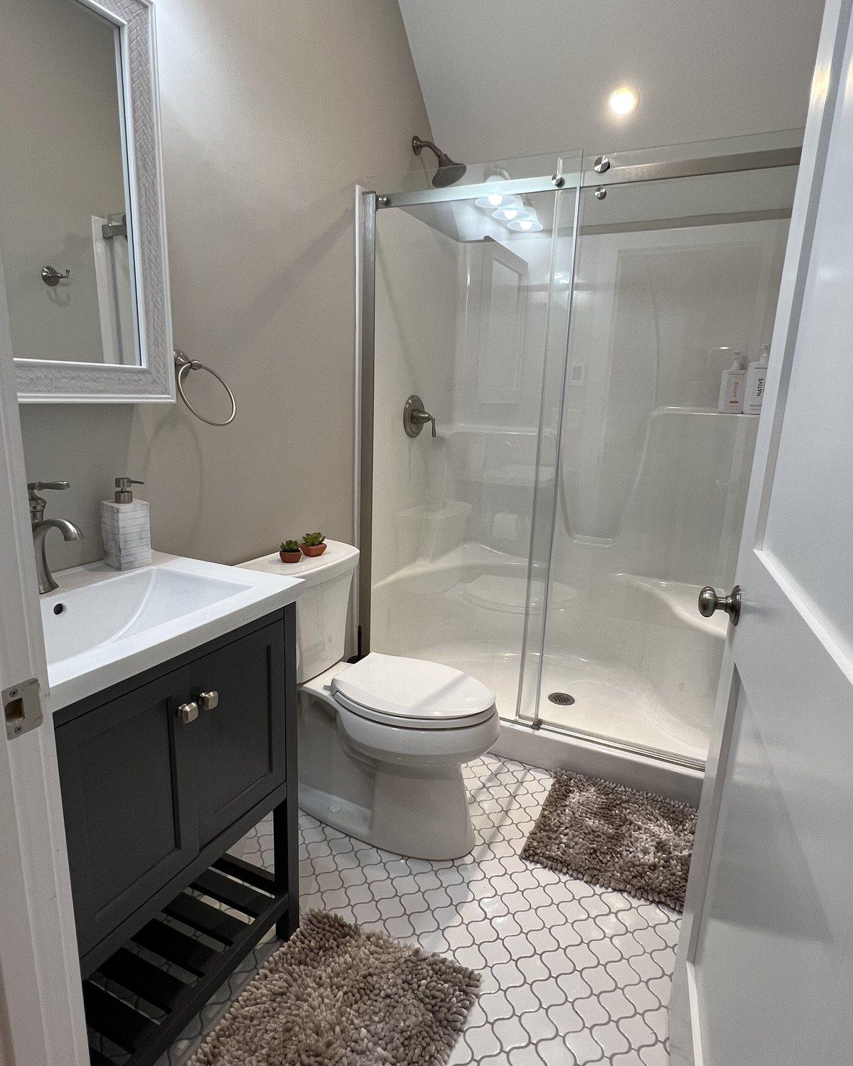 First-floor bathroom with a glass-door shower, vanity, and white tile floor.