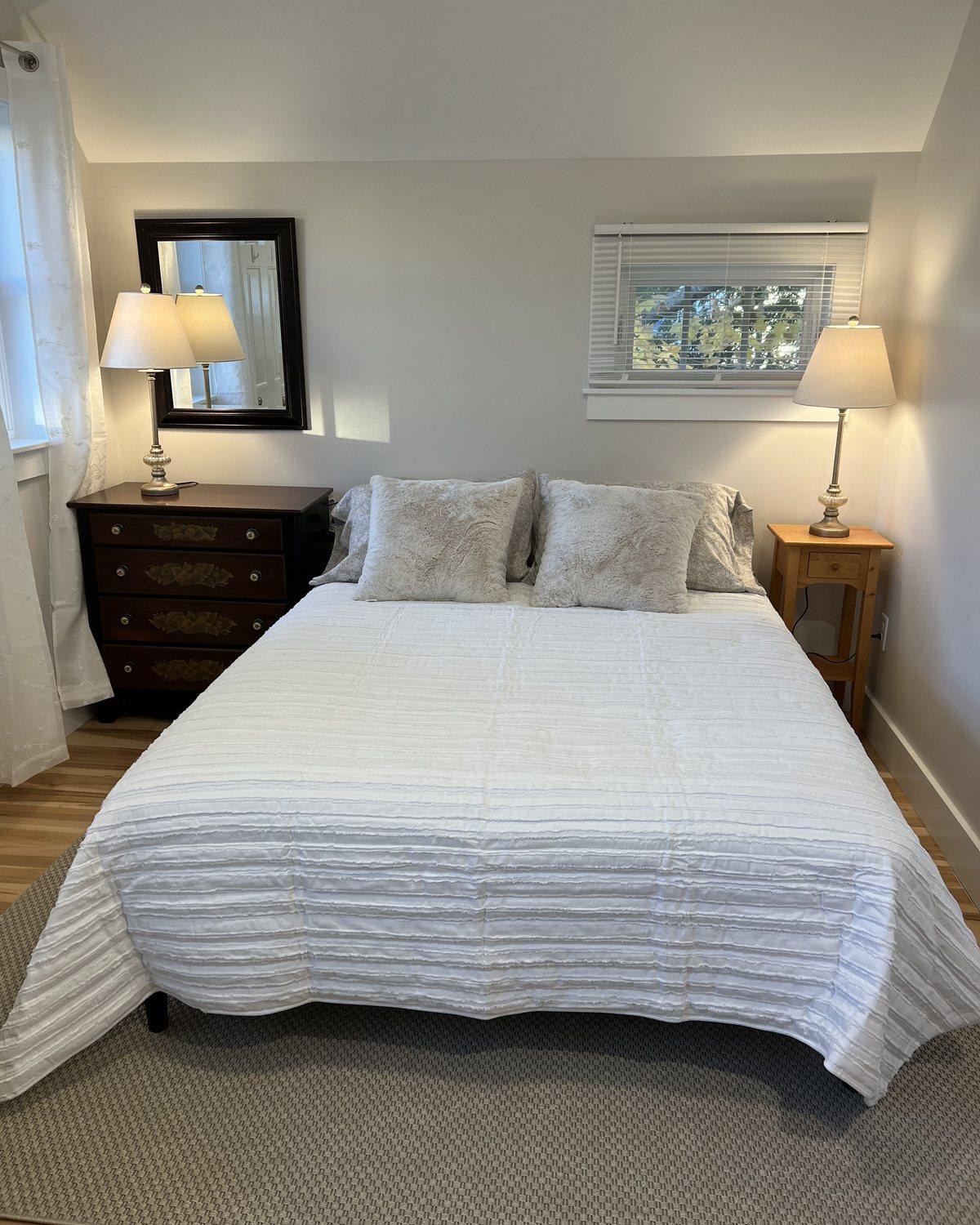 First-floor bedroom with a white-covered bed, two lamps, a dresser, and a small window.
