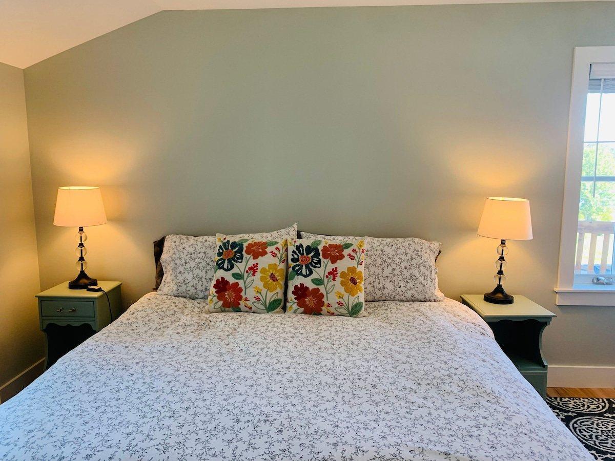 Upstairs bedroom with a floral-print bed, two lamps, and a window onto the balcony.